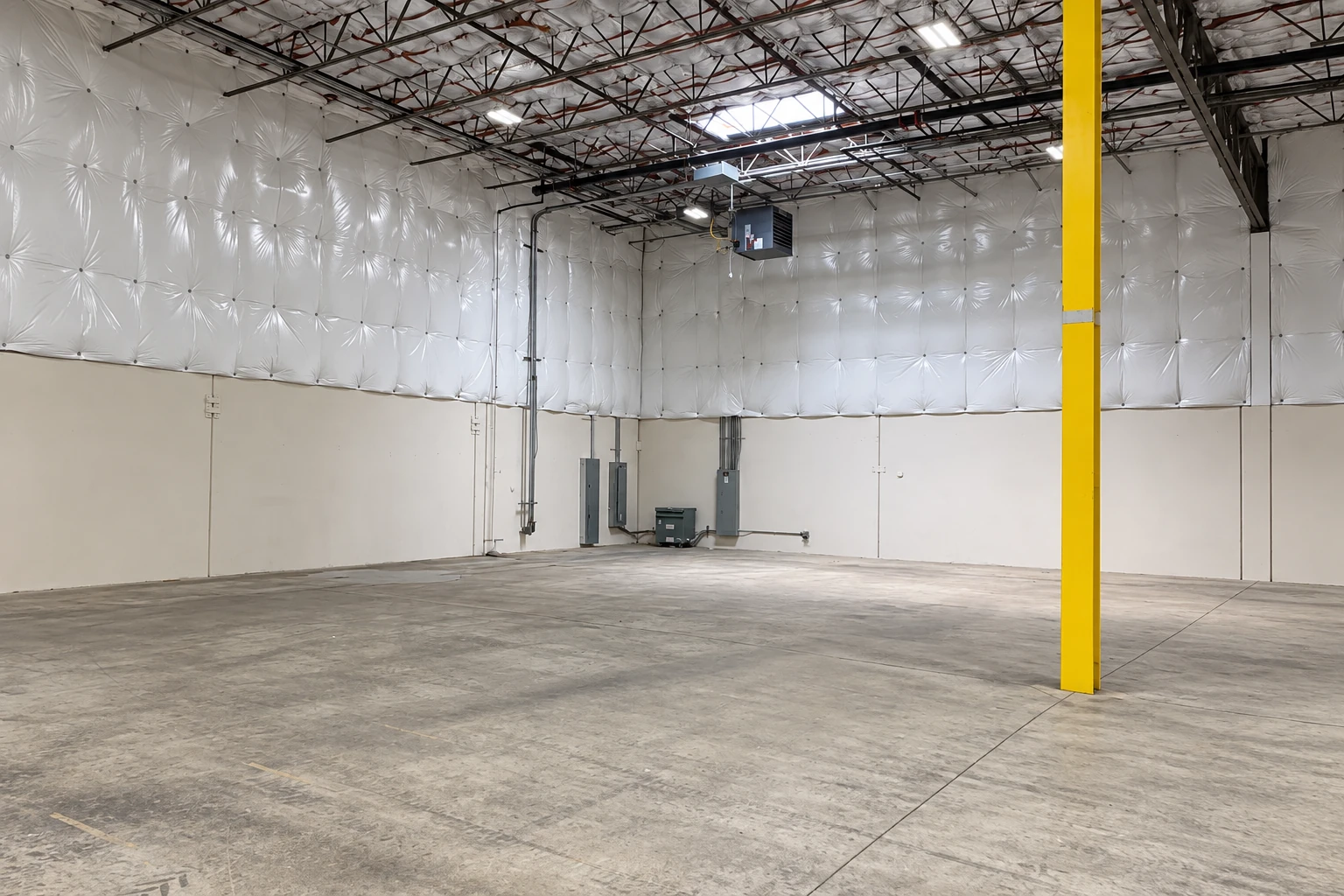 An empty commercial space has white insulation covering the upper walls and ceiling beneath exposed roof trusses.