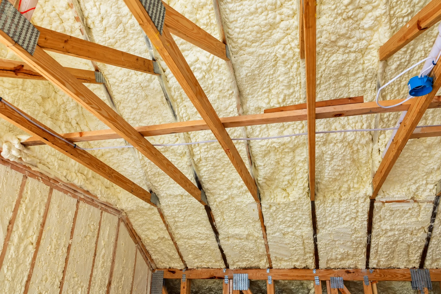 Spray foam insulation fills the roof cavities between exposed wooden rafters.